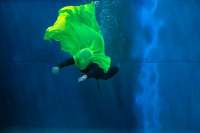 Grüner Farbklecks im blauen Wasser. Die Tänzer*innen spielen damit.