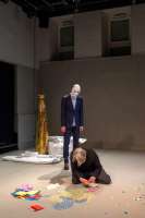 Robert Steijn legt ein Puzzle aus bunten Papierschnitzeln auf der Bühne. Ein Der Mann mit Maske vertreibt ihn und entpuppt sich als Frans Poelstra.