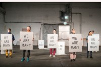 Alle sechs Mitwirkenden tragen eine Platte mit der gleichen Schrift: "We are manx" / "Wir sind viele". © Fanni Futterknecht.